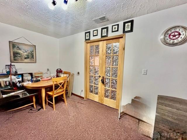 carpeted dining space with french doors, visible vents, and a textured ceiling