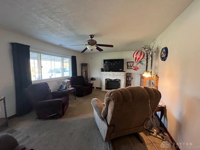 living room featuring carpet floors, ceiling fan, a textured ceiling, and a fireplace