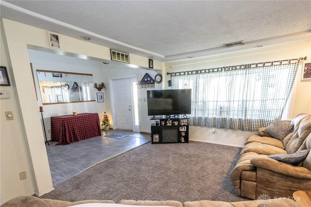 carpeted living area with visible vents, a wealth of natural light, and a textured ceiling