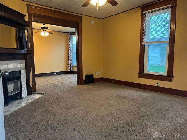 unfurnished living room featuring a large fireplace, a ceiling fan, carpet, and a healthy amount of sunlight