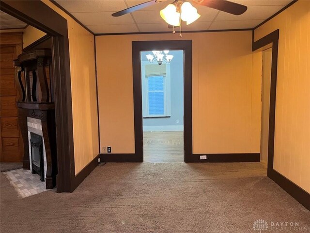 unfurnished room with carpet, crown molding, ceiling fan with notable chandelier, wood walls, and a drop ceiling