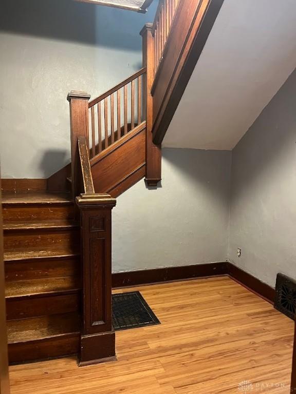 stairway featuring visible vents, baseboards, wood finished floors, and lofted ceiling
