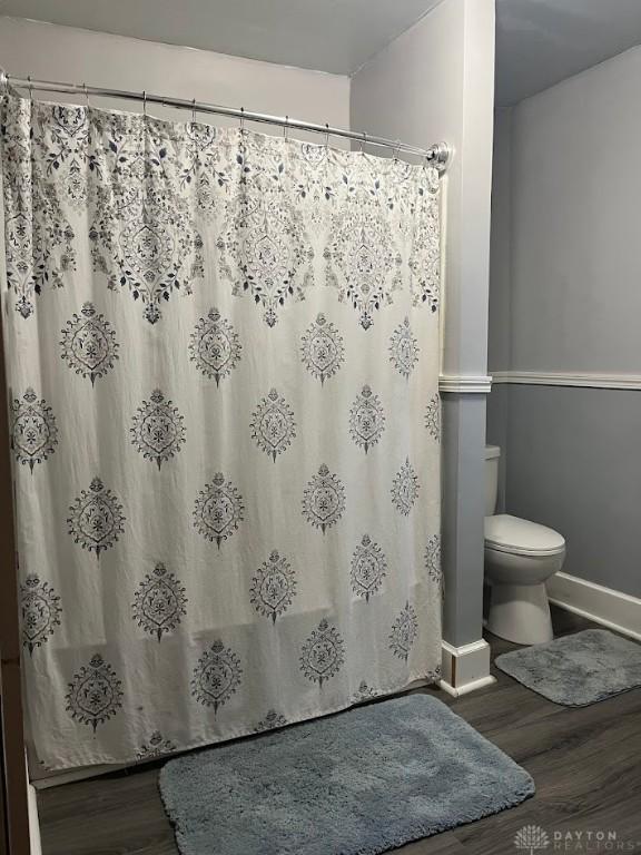 full bath featuring a shower with shower curtain, baseboards, toilet, and wood finished floors