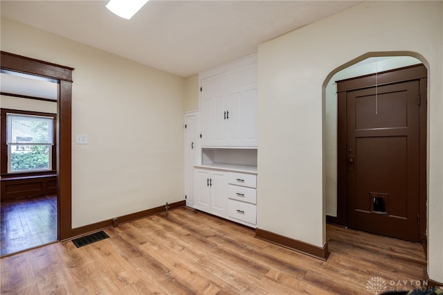 interior space featuring arched walkways, light wood finished floors, visible vents, and baseboards