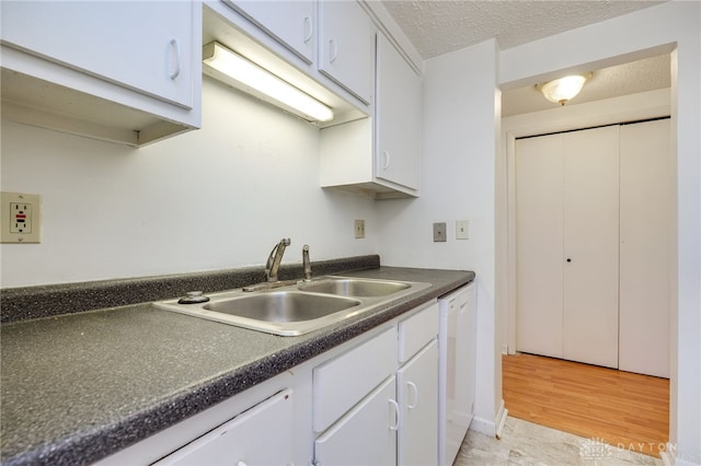 kitchen featuring a textured ceiling, white cabinetry, dark countertops, dishwasher, and a sink