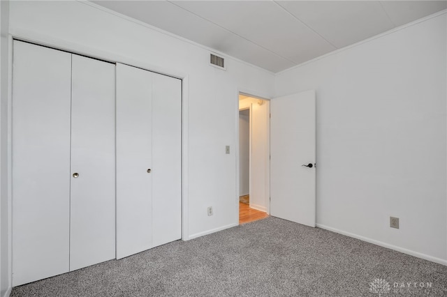 unfurnished bedroom with baseboards, a closet, ornamental molding, carpet floors, and visible vents