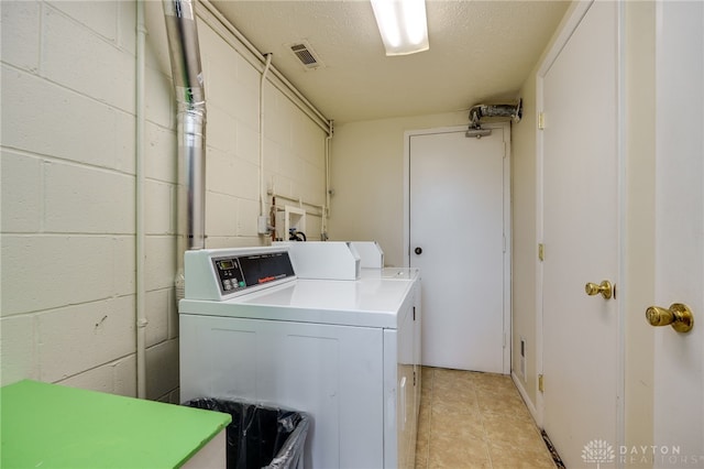 shared laundry area with visible vents, a textured ceiling, concrete block wall, washing machine and dryer, and light tile patterned flooring