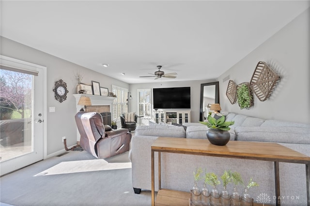 living room featuring baseboards, a fireplace, a ceiling fan, and carpet