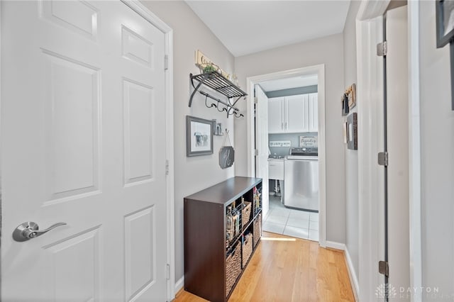 corridor featuring washer / clothes dryer, baseboards, and light wood-style floors
