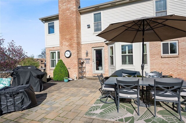 back of house featuring a chimney, a patio area, outdoor dining space, and brick siding