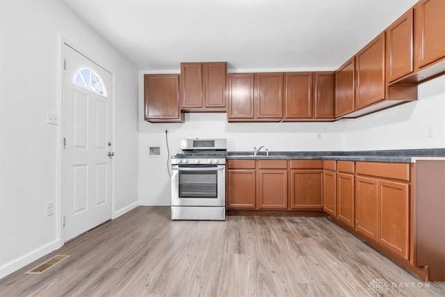 kitchen featuring visible vents, gas stove, a sink, brown cabinets, and light wood finished floors