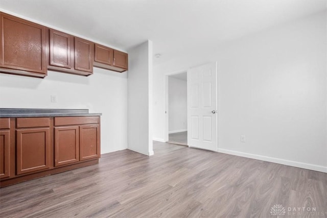 kitchen featuring brown cabinetry, light wood-style flooring, dark countertops, and baseboards