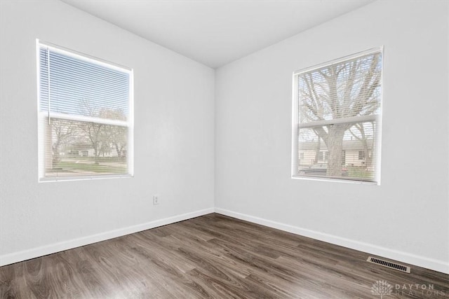empty room featuring wood finished floors, baseboards, and visible vents
