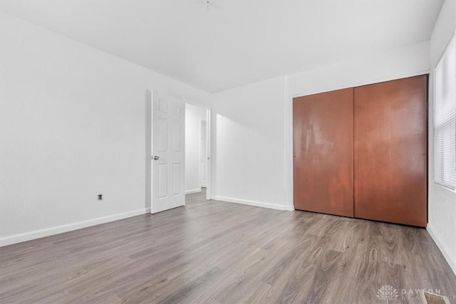 unfurnished bedroom featuring wood finished floors, baseboards, and a closet