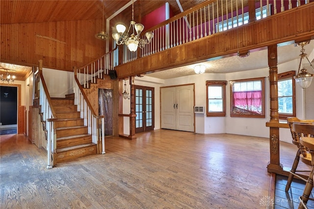 unfurnished living room with wood finished floors, high vaulted ceiling, an inviting chandelier, and stairway