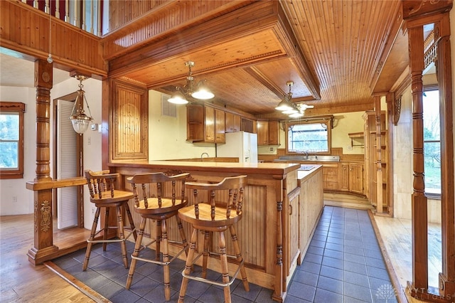 kitchen featuring white fridge with ice dispenser, a peninsula, wooden ceiling, light countertops, and decorative light fixtures