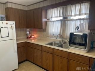 kitchen with light countertops, freestanding refrigerator, a sink, and brown cabinetry