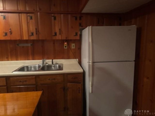 kitchen with light countertops, brown cabinets, freestanding refrigerator, and a sink