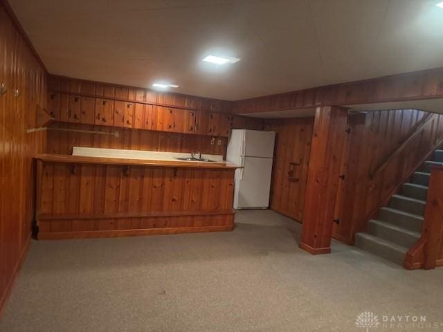 bar with light carpet, wood walls, freestanding refrigerator, and a sink
