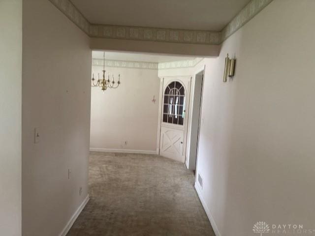 hallway with carpet floors, baseboards, and a chandelier