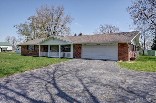 ranch-style home featuring covered porch, a garage, aphalt driveway, brick siding, and a front lawn
