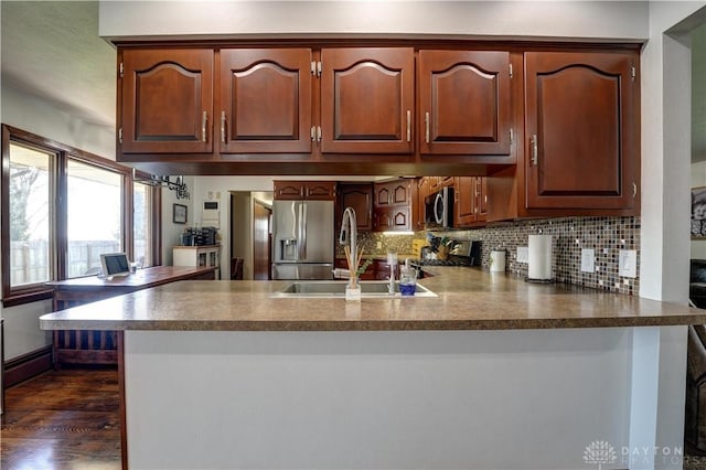kitchen featuring tasteful backsplash, a sink, a peninsula, stainless steel appliances, and dark wood-type flooring