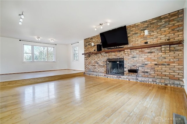 unfurnished living room featuring visible vents, a brick fireplace, wood finished floors, and baseboards