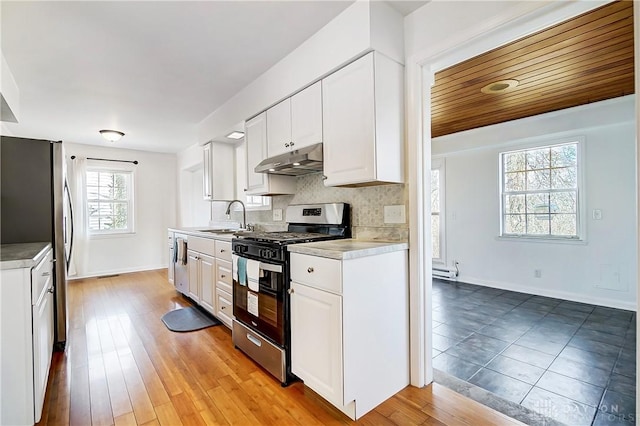 kitchen with backsplash, white cabinets, under cabinet range hood, appliances with stainless steel finishes, and a sink
