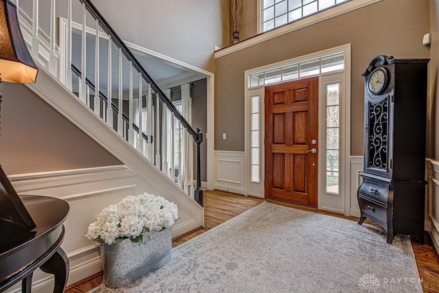 entrance foyer featuring a towering ceiling, a wainscoted wall, stairs, a decorative wall, and wood finished floors