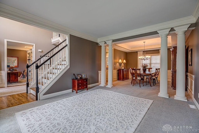 carpeted entryway featuring visible vents, a notable chandelier, ornamental molding, ornate columns, and stairs