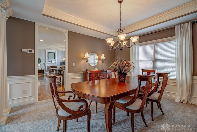 dining room featuring a decorative wall, a tray ceiling, ornamental molding, and a wainscoted wall