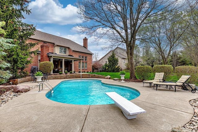 outdoor pool with a diving board and a patio area