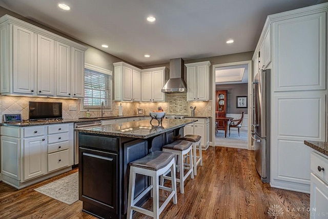 kitchen with dark wood-style flooring, wall chimney exhaust hood, high end fridge, and a breakfast bar