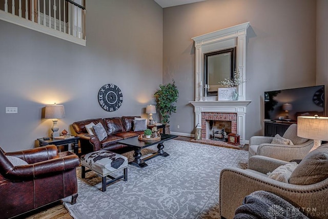 living area with a towering ceiling, a brick fireplace, baseboards, and wood finished floors