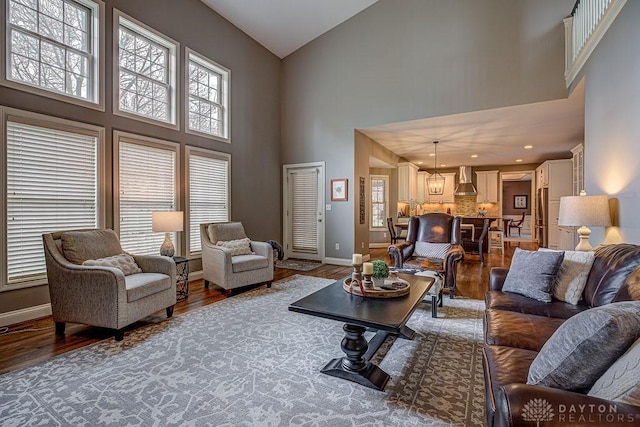 living room featuring wood finished floors, high vaulted ceiling, baseboards, and an inviting chandelier