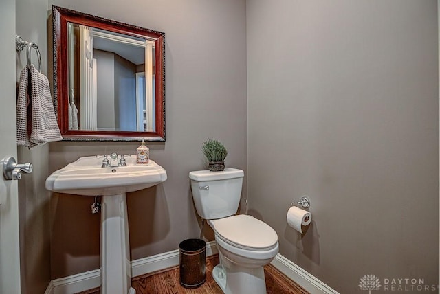 half bathroom with toilet, wood finished floors, and baseboards