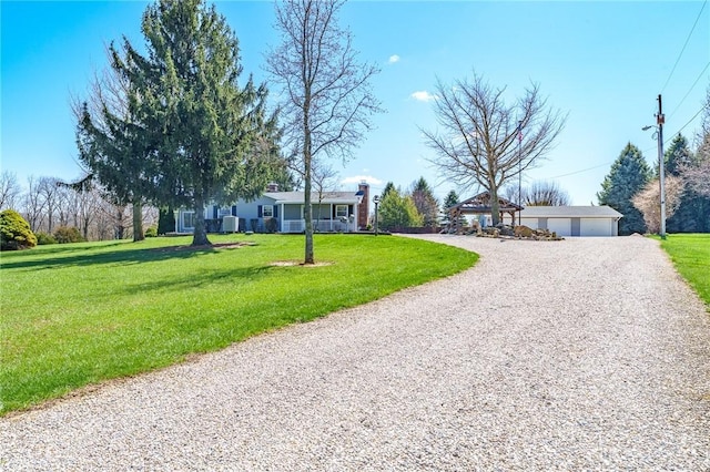 view of front of home featuring a front yard, gravel driveway, and a detached garage