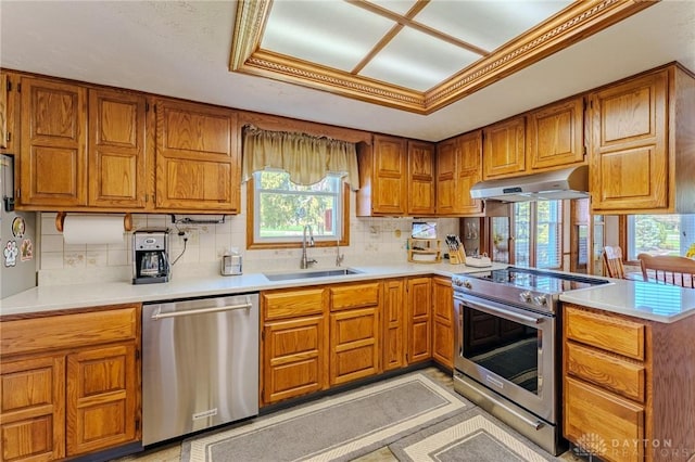 kitchen with a peninsula, under cabinet range hood, brown cabinets, appliances with stainless steel finishes, and a sink