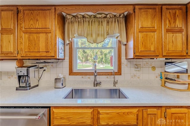 kitchen with light countertops, brown cabinets, decorative backsplash, stainless steel dishwasher, and a sink