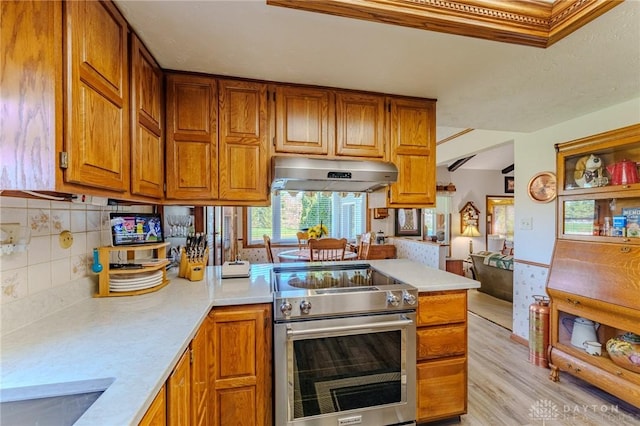 kitchen with light wood-type flooring, stainless steel electric range oven, under cabinet range hood, light countertops, and brown cabinets