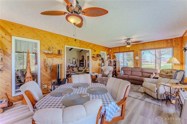 dining area with light wood finished floors, a textured ceiling, wooden walls, and a ceiling fan