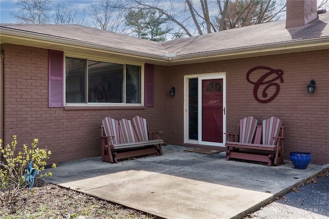 property entrance with a patio area, brick siding, and a chimney