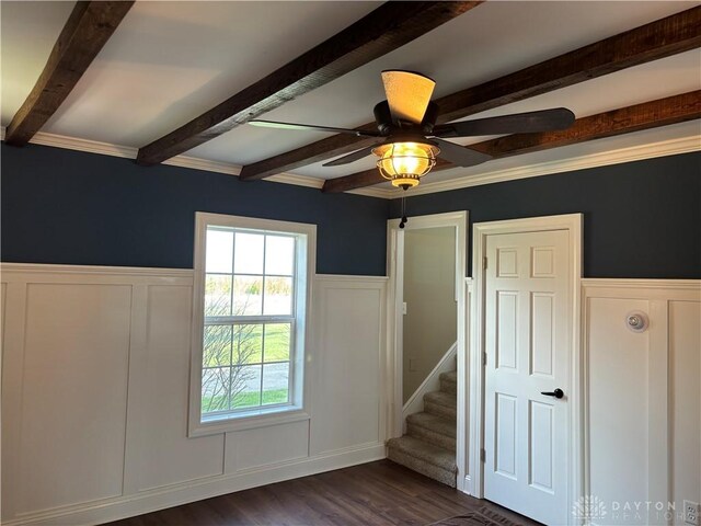unfurnished bedroom with a decorative wall, beam ceiling, a wainscoted wall, and dark wood-type flooring