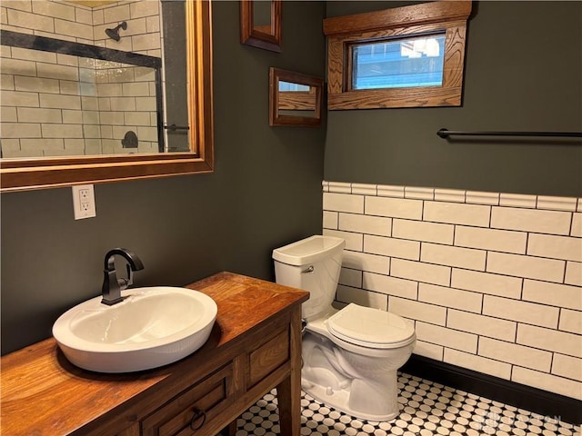 bathroom featuring vanity, toilet, tiled shower, wainscoting, and tile walls