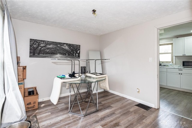 office featuring baseboards, light wood-style flooring, a textured ceiling, and visible vents