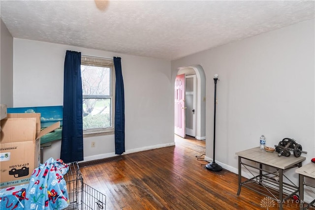 interior space featuring arched walkways, hardwood / wood-style flooring, baseboards, and a textured ceiling