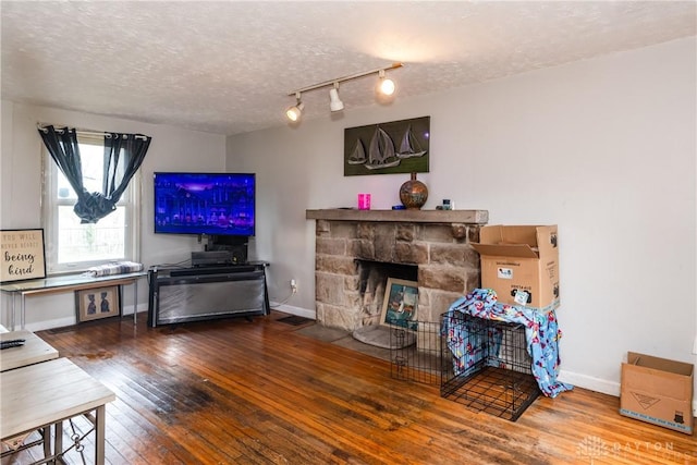 living area featuring baseboards, a stone fireplace, a textured ceiling, and hardwood / wood-style floors