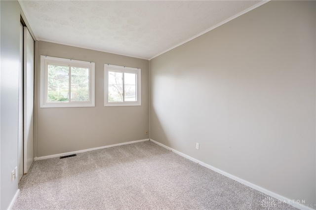 empty room featuring ornamental molding, baseboards, visible vents, and carpet flooring