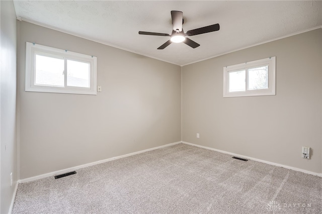 spare room with a ceiling fan, baseboards, ornamental molding, carpet flooring, and visible vents