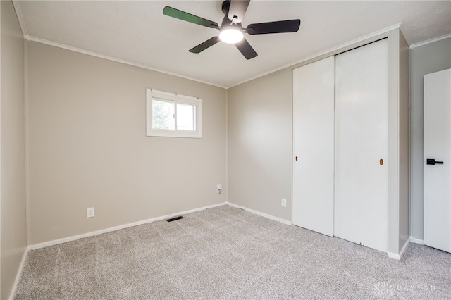 unfurnished bedroom with carpet, visible vents, a closet, crown molding, and baseboards